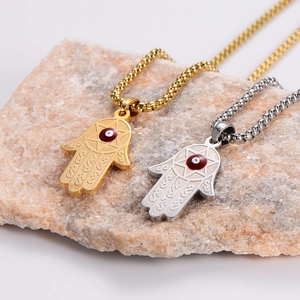 Gold and silver Hamsa Hand evil eye necklaces on a textured natural stone base