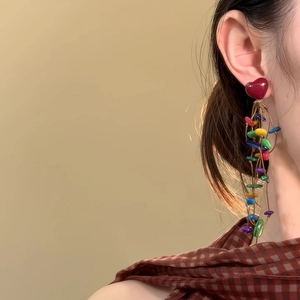 Detail of colorful long tassel heart earrings with vibrant beads on a female model