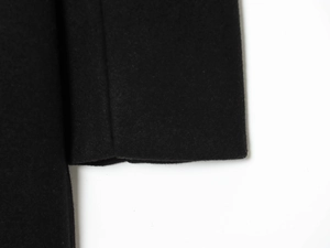 Detailed close-up of premium wool blend texture and stitching on black coat sleeve cuff