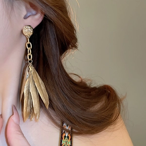 Detail of vintage gold feather tassel earrings on a model showing bohemian texture