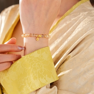 Detail of beaded citrine bracelet with gold fortune charms on silk fabric background