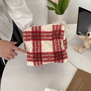 Detailopname van rood en beige geruite sherpa-tas vastgehouden in een huiselijke sfeer