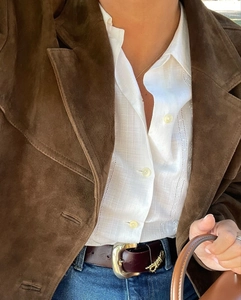 Close-up of brown suede blazer layered over white hollow stripe shirt with leather belt