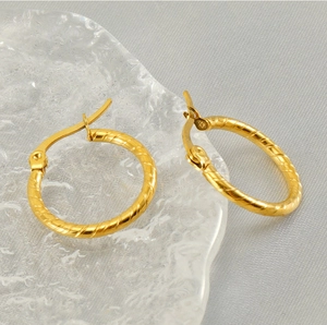Detailed macro view of gold-tone twisted hoop earrings crafted from 18k stainless steel