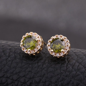 Détail de boucles d'oreilles dorées avec zircon vert sur fond de cuir noir texturé