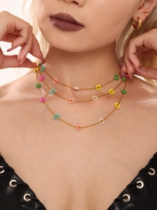 Close-up of layered gold necklaces with colorful beads and flower charms on a model