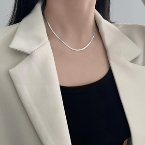 Minimalist silver flat snake bone chain necklace worn by a model in a beige suit
