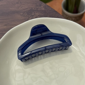 Deep blue translucent hair claw clip with non-slip teeth shown on a ceramic plate