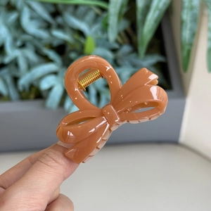 Macro view of caramel bow hair claw clip made of glossy acrylic and golden metal spring