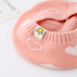 Close-up of pink knitted baby beret with white heart patterns and crown logo tag