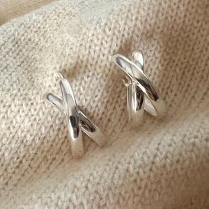 Detailed close-up of silver S925 sterling silver knot earrings on a cozy beige background