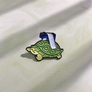 Detailed view of creative green turtle enamel pin with blue camera on light grey surface