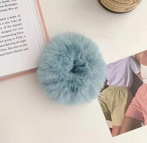 Detail of a fluffy plush scrunchie in light mint green on a white desk with props