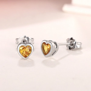Macro view of dainty S925 silver earrings with heart-cut yellow gemstone settings