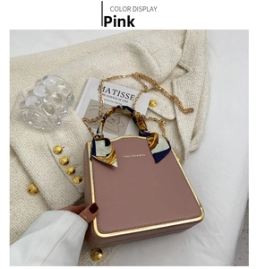 Pink box bag with silk scarf handle and gold chain detail on textured white fabric