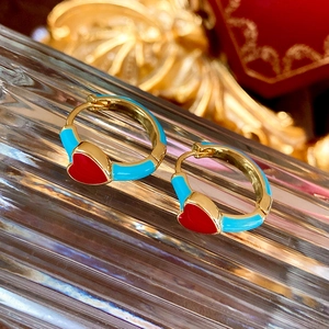 Detail von goldenen Herzohrringen mit roter und blauer Emaille auf Glasoberfläche