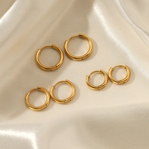Three pairs of gold stainless steel hoop earrings in different sizes on silk fabric