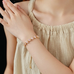 Detail of double-layer golden bracelet with pink heart-shaped zircons and adjustable pull ball