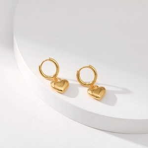 Polished 18K gold plated heart charm hoop earrings shown on a white pedestal