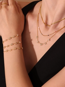 Détail d'un ensemble de bijoux MAMA dorés avec pendentifs zircon et perles colorées
