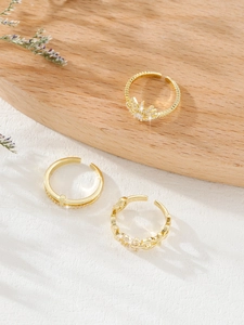 Detailed view of three gold-plated open rings with cubic zirconia on a wooden tray