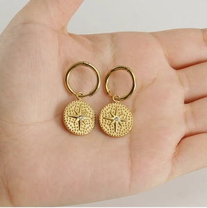 Macro detail of 18K gold-plated hoop earrings with starburst engraved coin charms
