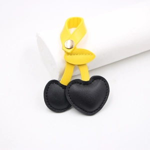 Close-up of retro leather cherry bag charm with black heart-shaped fruits and yellow leaf