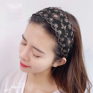 Elegante diadema ancha negra con bordado floral dorado y cuentas en una modelo