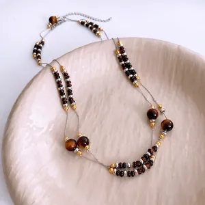 Double-layered tiger eye stone and pearl necklace draped on a ceramic tray
