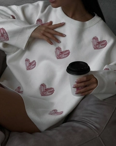 Detail of white knit sweater featuring red heart jacquard and cozy long sleeve design