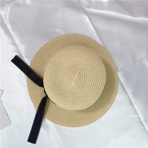 High-angle close-up detail of a beige woven straw sun hat with a chic black bow ribbon