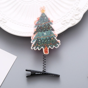Funkelnde grüne Weihnachtsbaum-Haarklammer mit Feder auf einem weißen Dekoteller