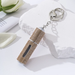 Detail of a golden diamond-studded perfume atomizer with a keychain and white rose decor