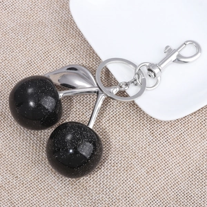 Detail view of sparkly black cherry keychain with silver leaves and lobster clasp on texture