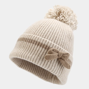 Detailed knit texture of a beige winter hat with a brown bow and fluffy pom-pom