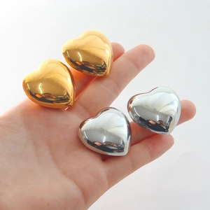 Polished heart-shaped stud earrings in gold and silver held by hand for scale