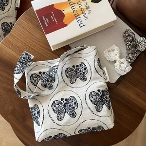 Off-white cotton tote bag with butterfly embroidery and a small brand label on wood table