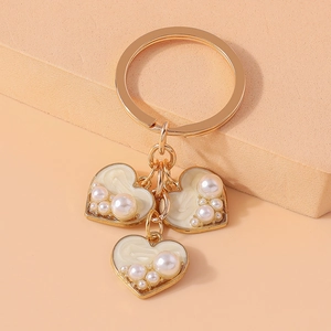 Close-up of golden heart-shaped pendants with white resin and pearls on a keychain