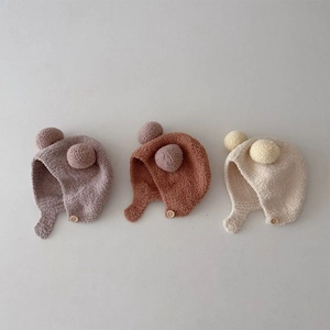 Detail view of knit baby earflap hats with pom-poms and wood buttons in multiple colors