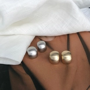 Orecchini geometrici minimalisti color oro e argento su elegante tessuto di seta marrone