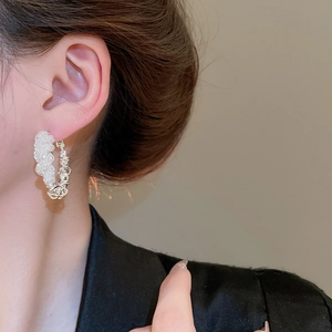Detail view of a model wearing C-shaped silver mesh earrings with beaded textures