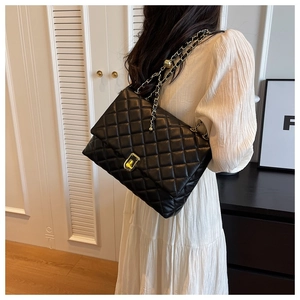 Detail of black quilted shoulder bag featuring golden ball chain and adjustable strap