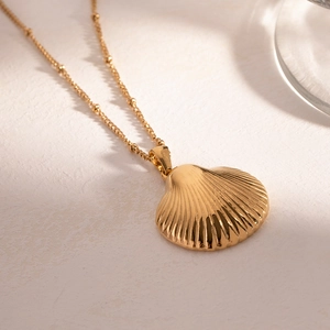 Detailed close-up of a gold shell pendant on a fine bead chain over a textured surface