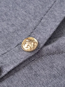 Close-up of golden embossed button on grey soft knit cardigan sweater garment texture