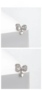 Detail of silver bow stud earring with heart charm and opal stone on white display