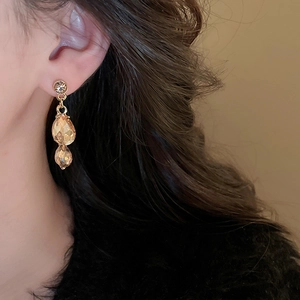 Close-up of elegant gold earrings with amber teardrop crystals worn by a model