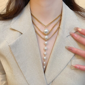 Detail of layered gold Y-necklace with elegant cascading pearls on beige suit