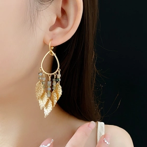Gros plan de boucles d'oreilles dorées en forme de goutte d'eau avec glands de feuilles sur modèle