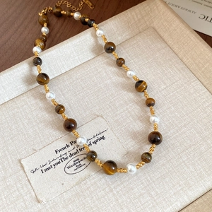 Macro detail of tiger eye beads and pearls on a gold-plated stainless steel floral necklace