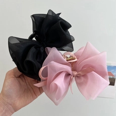 Detail of pink and black hair claw clips with large sheer gauze bows held in hand
